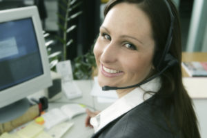 Woman with headset smiling at her computer.