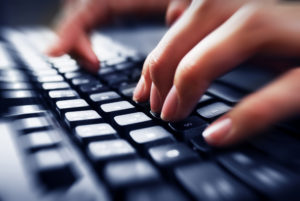 Woman's fingers typing at a black keyboard.