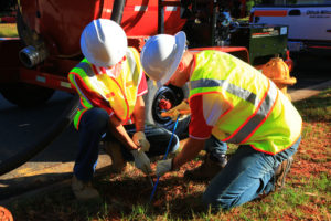 Two technicians assessing the ground outside with tools.