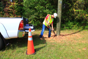 Technician outside testing the base of a wooden pole.
